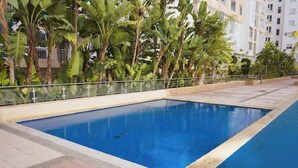 A rectangular swimming pool with a clear blue water surface, surrounded by a tiled deck and a metal railing. - Fully-equipped studio, pool view. (Agadir)