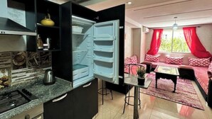 A compact living space with a kitchen area featuring a stove and a refrigerator. There is a dining table with chairs and a sofa with red curtains. - Fully-equipped studio, pool view. (Agadir)