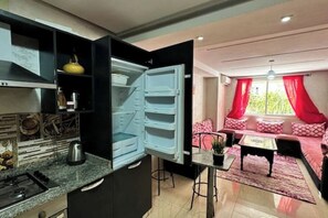 A compact living space with a kitchen area featuring a stove and a refrigerator. There is a dining table with chairs and a sofa with red curtains.
