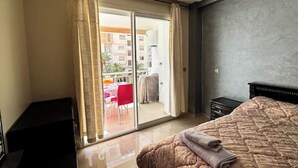 A bedroom with a large bed, a sliding glass door to a balcony, and a dark-colored dresser. - Fully-equipped studio, pool view. (Agadir)