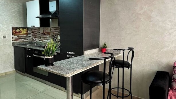 A modern kitchen with black cabinets, a granite countertop, and two black bar stools. - Fully-equipped studio, pool view. (Agadir)