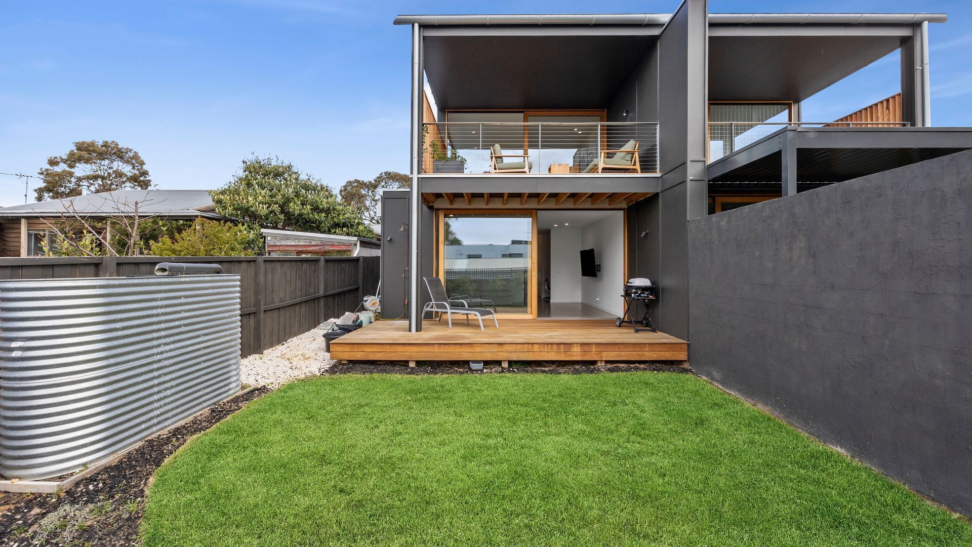 A modern two-story house with a balcony, a wooden deck, and a well-maintained lawn.