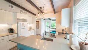 A modern kitchen with white cabinetry, a central island, and a hanging light fixture. - Crafted by a shipwright. Anchored in time. The Shipwright's Bungalow sleeps 9 (St Simons Island)