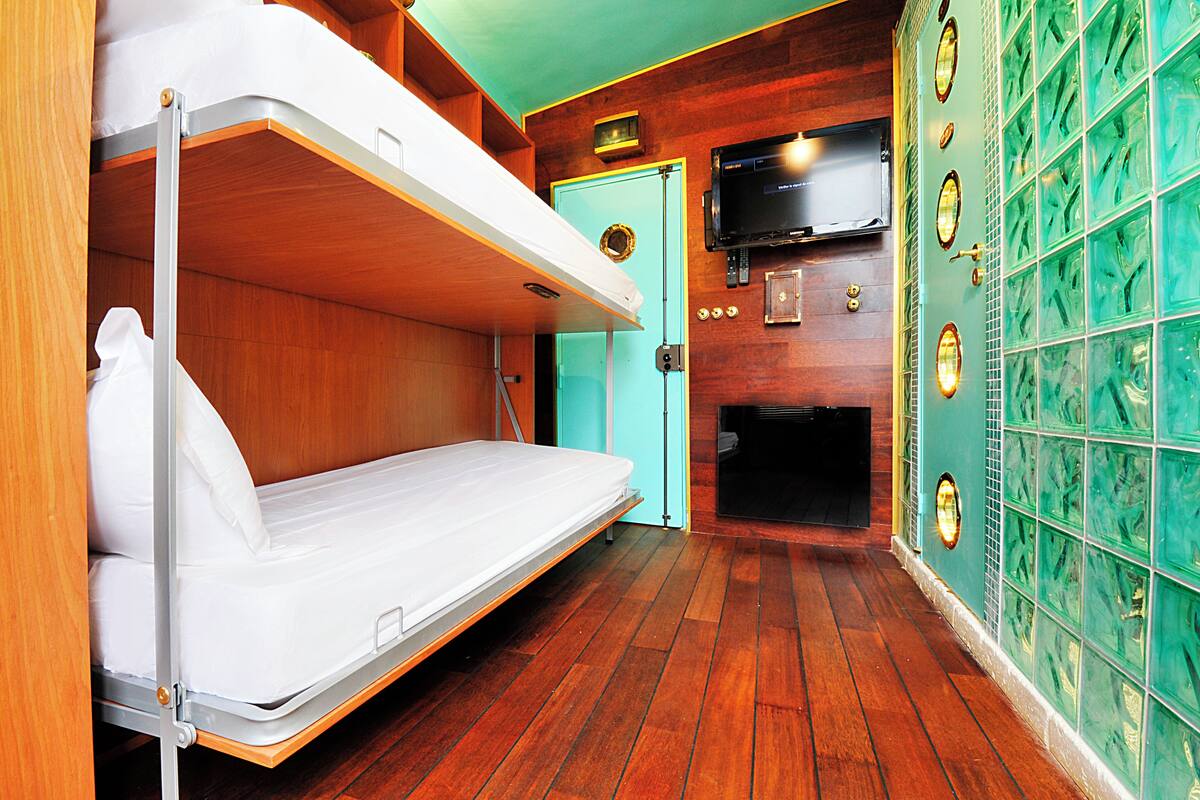 Une chambre compacte avec un lit superposé, une petite salle de bain avec douche et un téléviseur fixé au mur.