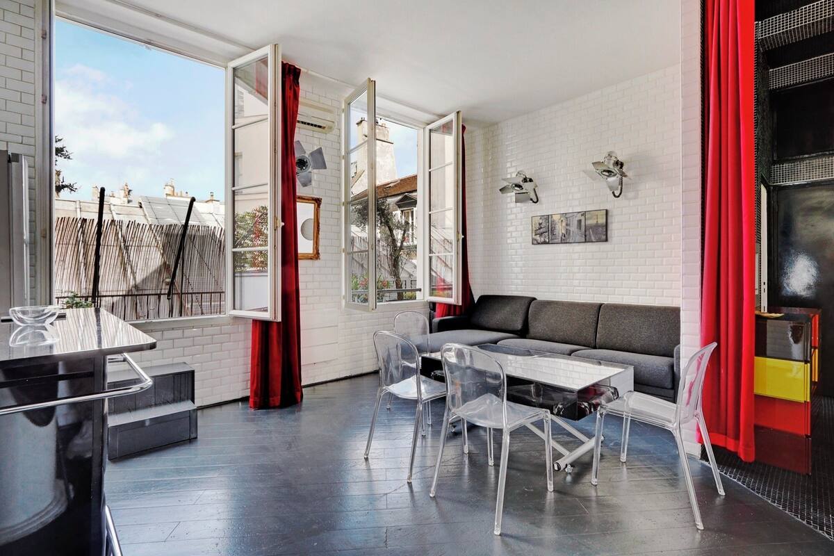 Un salon moderne avec un canapé, des chaises transparentes, une table à manger et un rideau rouge.
