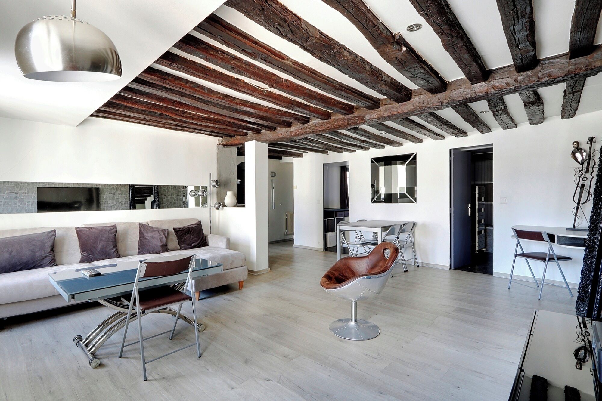 Una sala de estar moderna con vigas de madera a la vista, un sofá, una mesa de comedor y un taburete de bar.