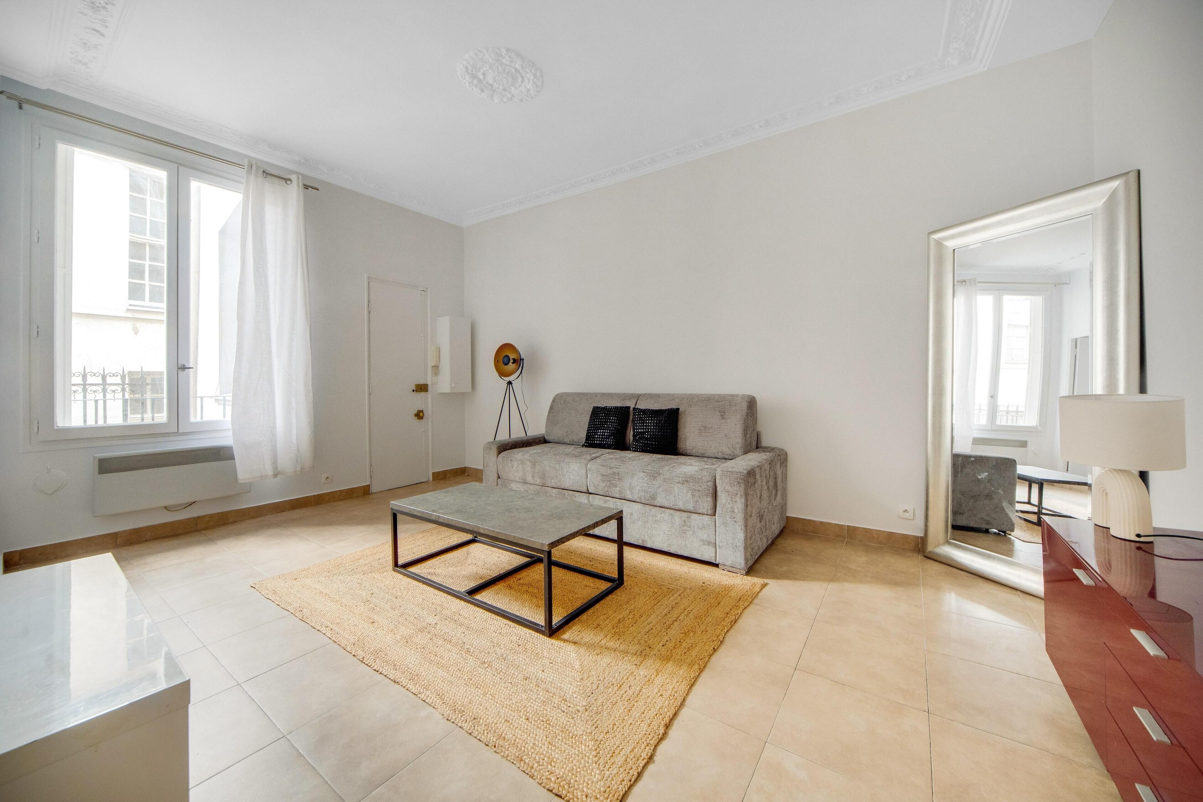 A spacious living room with a sofa, a coffee table, and a large mirror.