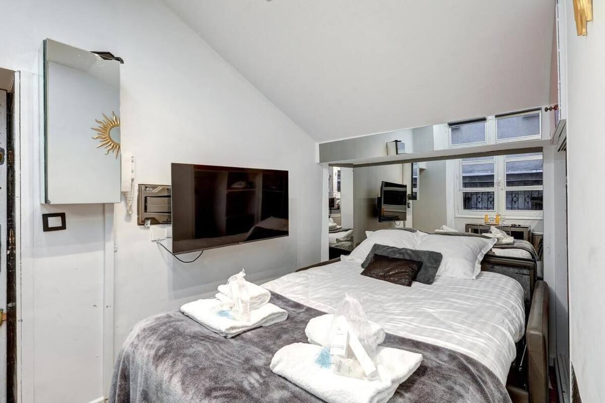Une chambre d’hôtel moderne dotée d’un grand lit, d’un téléviseur à écran plat, d’un miroir en forme de soleil et d’une fenêtre avec des rideaux.