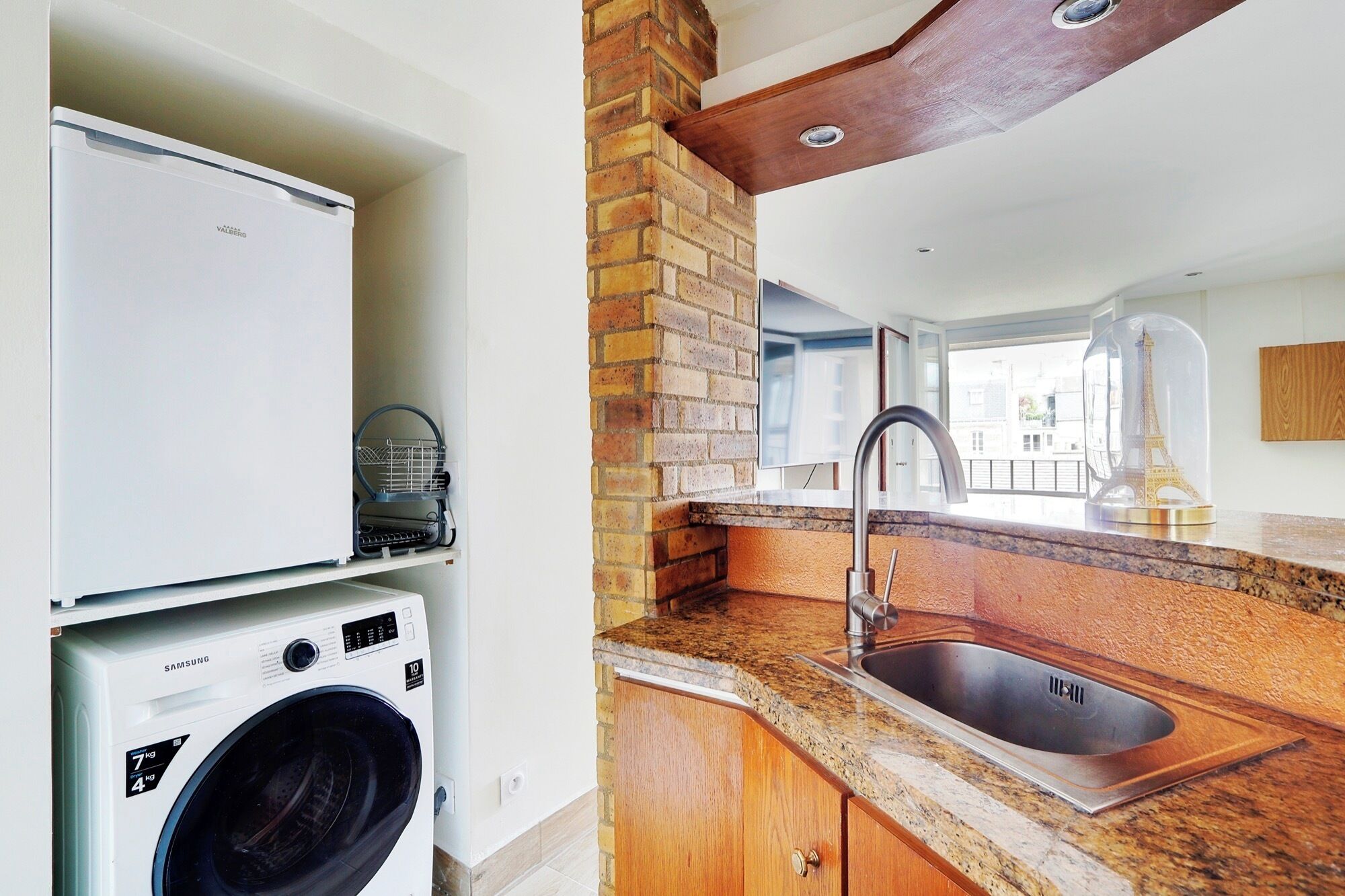 Una cocina con lavadora integrada, un lavabo y una pared de ladrillo.