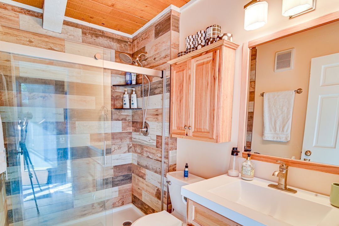 Une salle de bain avec une cabine de douche en bois, un lavabo blanc et un miroir au-dessus.