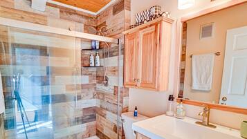 Une salle de bain avec une cabine de douche en bois, un lavabo blanc et un miroir au-dessus.