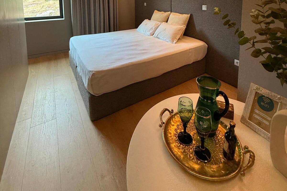 A modern hotel room with a large bed, a bedside table with a tray, and a window with curtains.
