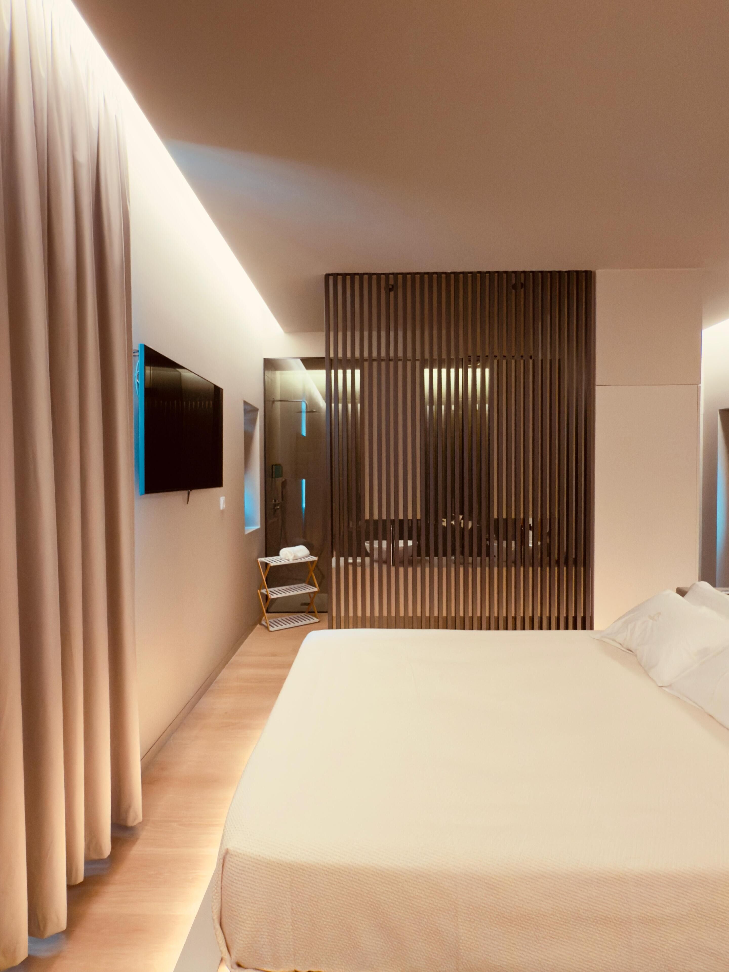 A modern hotel room with a large bed, a TV mounted on the wall, and a wooden partition.