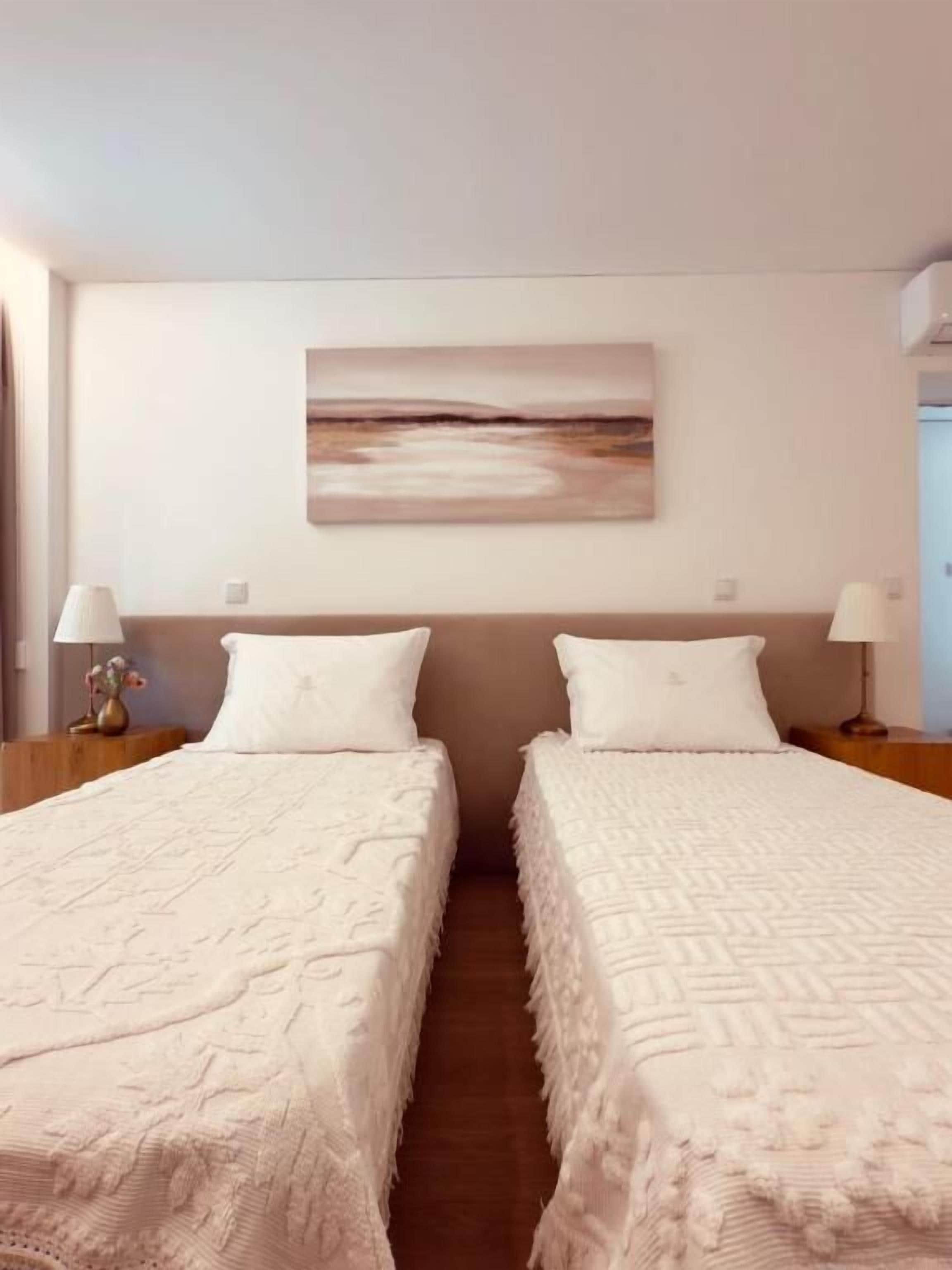 Hotellihuone, jossa on kaksi sänkyä, seinällä taulu ja yöpöydillä lamput.