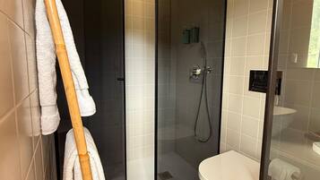 Uma casa de banho moderna com cabine de chuveiro em vidro, sanita e um porta-toalhas com vários toalhetes.