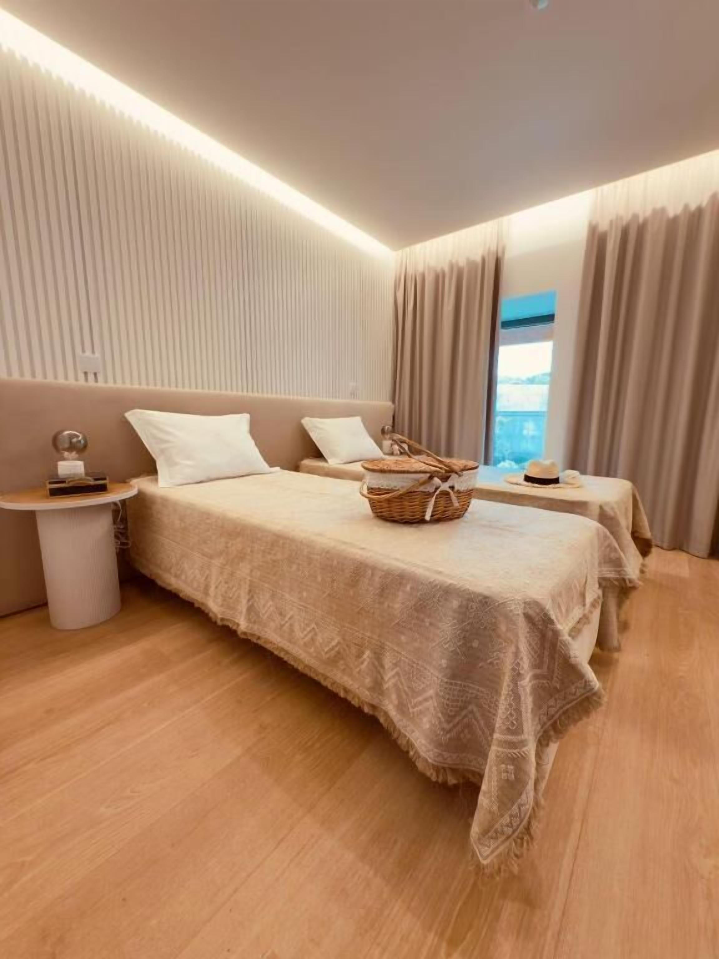 Habitación de hotel moderna con dos camas, una mesita de noche y vistas al exterior.