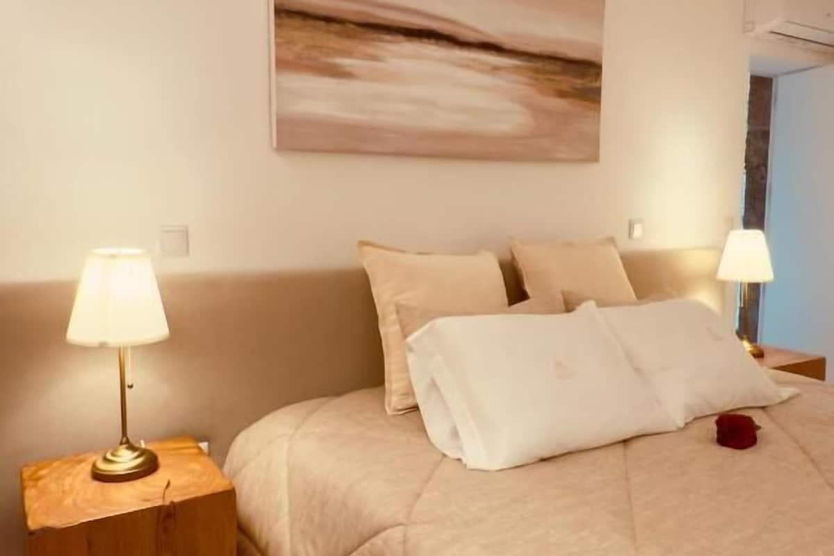 A neatly made bed with a quilted cover, two bedside lamps, and a single rose on the bed.