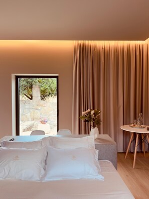 Habitación de hotel con cama, una mesita con un florero y vistas a un muro de piedra y follaje.