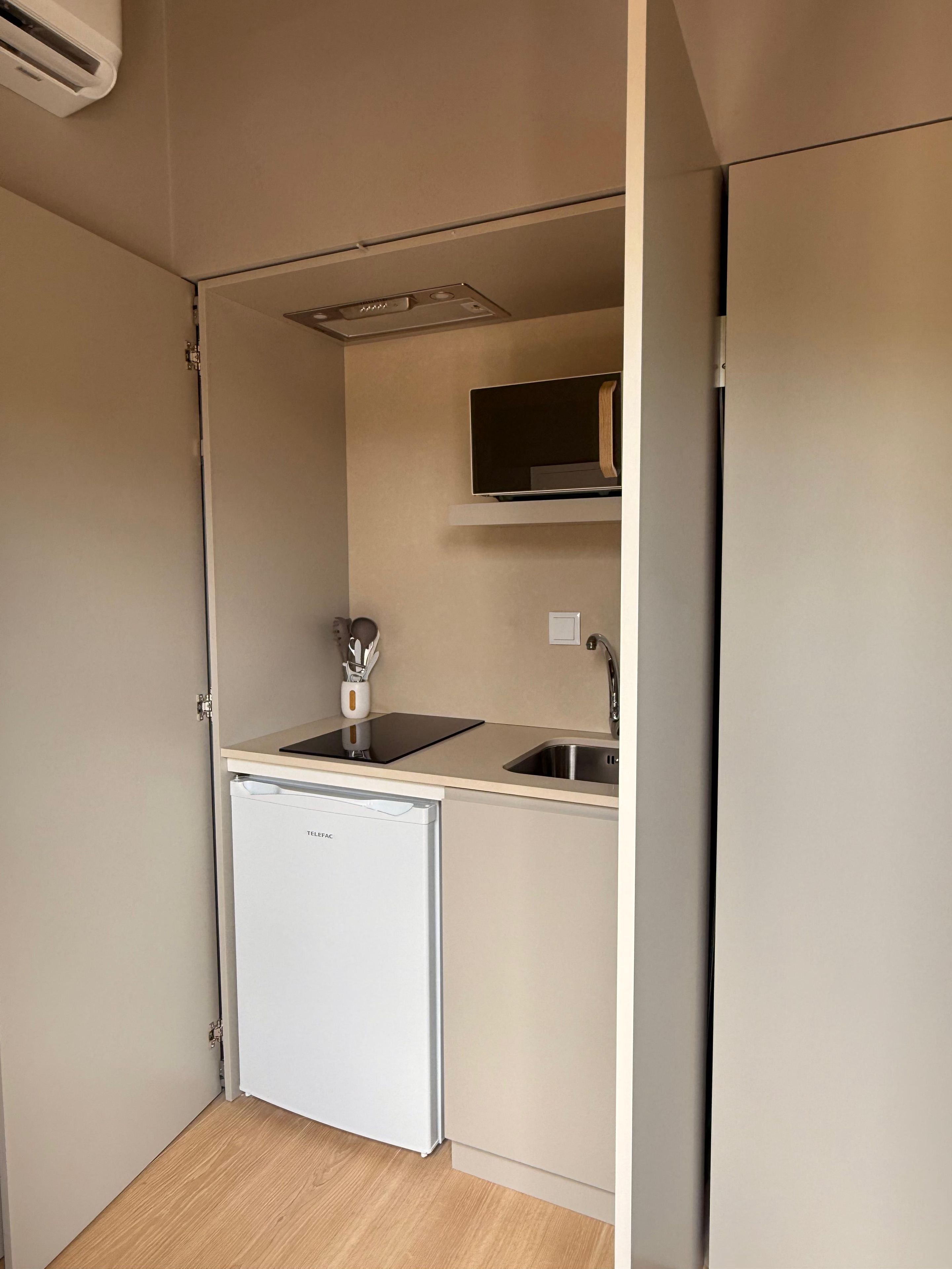 A compact kitchenette with a built-in refrigerator, a small sink, and a microwave.