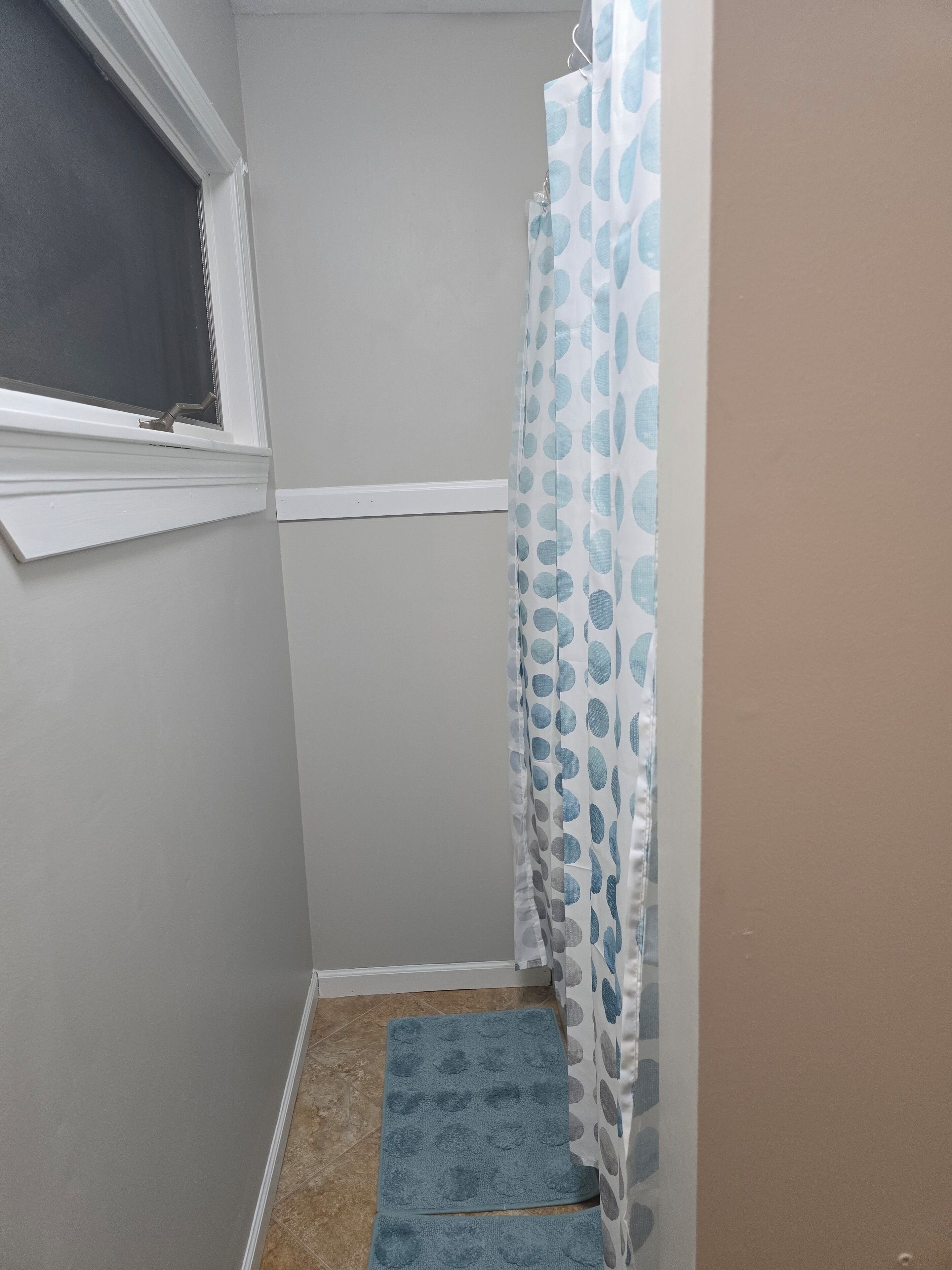 Ein kleines Badezimmer mit Dusche, einem Fenster und einer blauen Matte auf dem Boden.