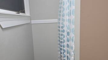 Ein kleines Badezimmer mit Dusche, einem Fenster und einer blauen Matte auf dem Boden.