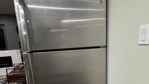 A stainless steel refrigerator in a kitchen with a wooden floor and a white wall.