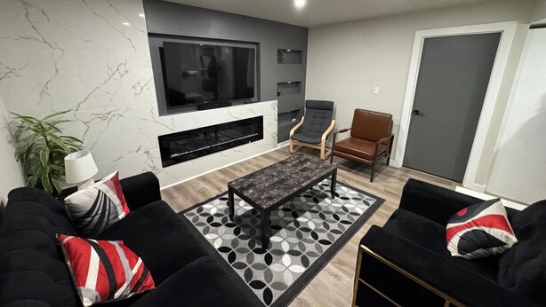 A modern living room with a large flat-screen TV, a fireplace, two sofas, and a coffee table.