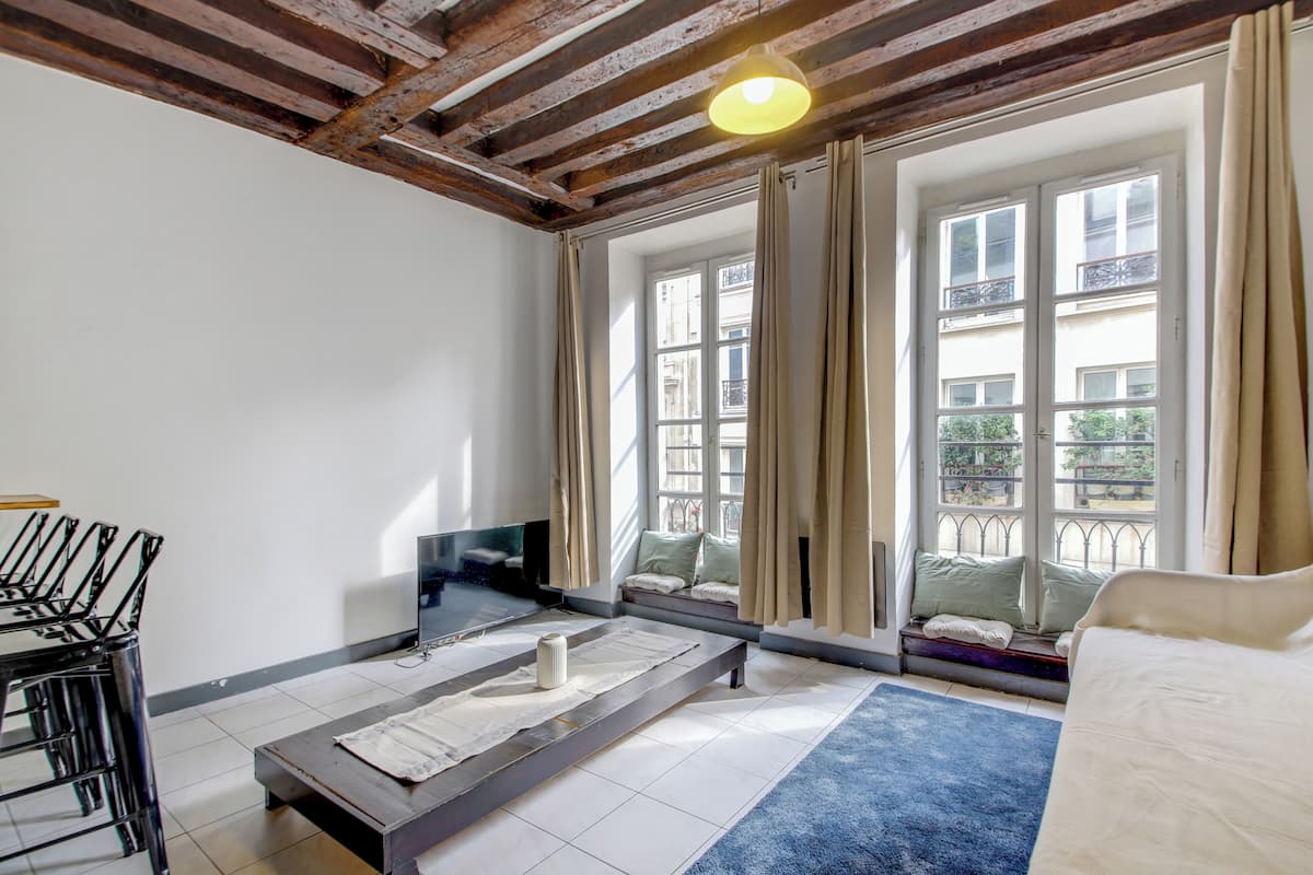 A room with a bed, a TV, a bench, and a window with curtains.
