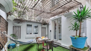 Eine kleine Terrasse mit Tisch und Stühlen, einer Hängematte und einem großen Kübelpflanzen.