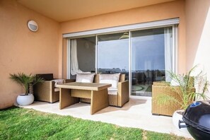 A balcony with wicker furniture, a barbecue grill, and potted plants.