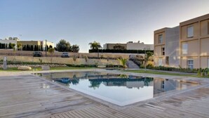 A modern pool area with a wooden deck, surrounded by buildings and greenery.