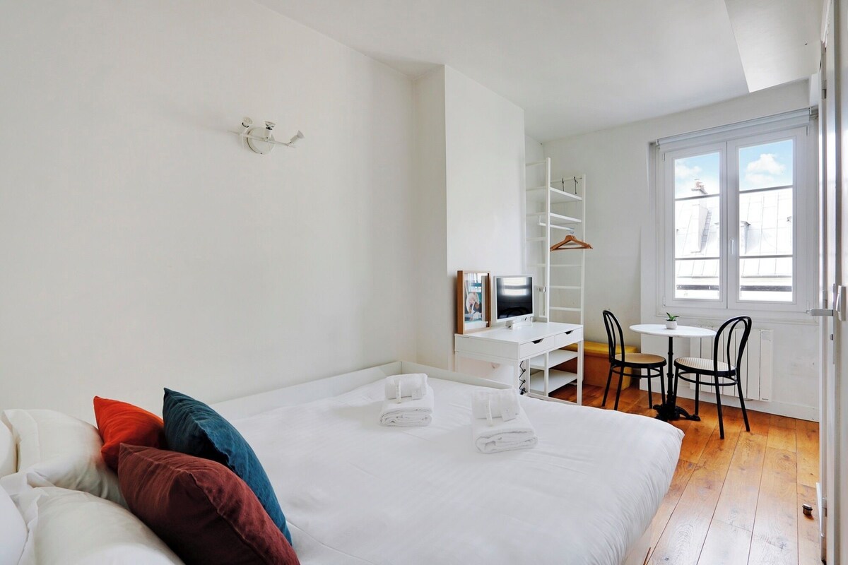 A bedroom with a bed, a desk, a chair, and a window.