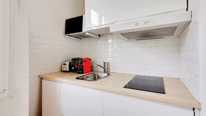 A compact kitchen with white cabinets, a stainless steel sink, a black induction cooktop, and a red appliance on the countertop. - 196LAFAYETTE (Paris)