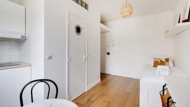 A compact kitchen with a stove, a white door, and a wooden floor. - 196LAFAYETTE (Paris)