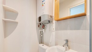 A bathroom with a white sink, a toilet, and a shower area. There are pipes and a water heater visible on the wall. - 196LAFAYETTE (Paris)
