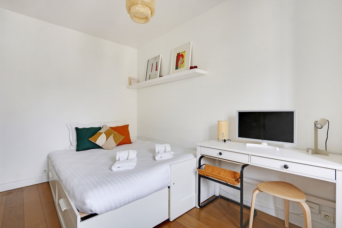 A modern bedroom with a bed, a desk, a chair, a television, and a shelf with pictures.
