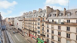 A row of multi-story buildings with balconies, a street with cars and pedestrians, and a clear sky. - 196LAFAYETTE (Paris)