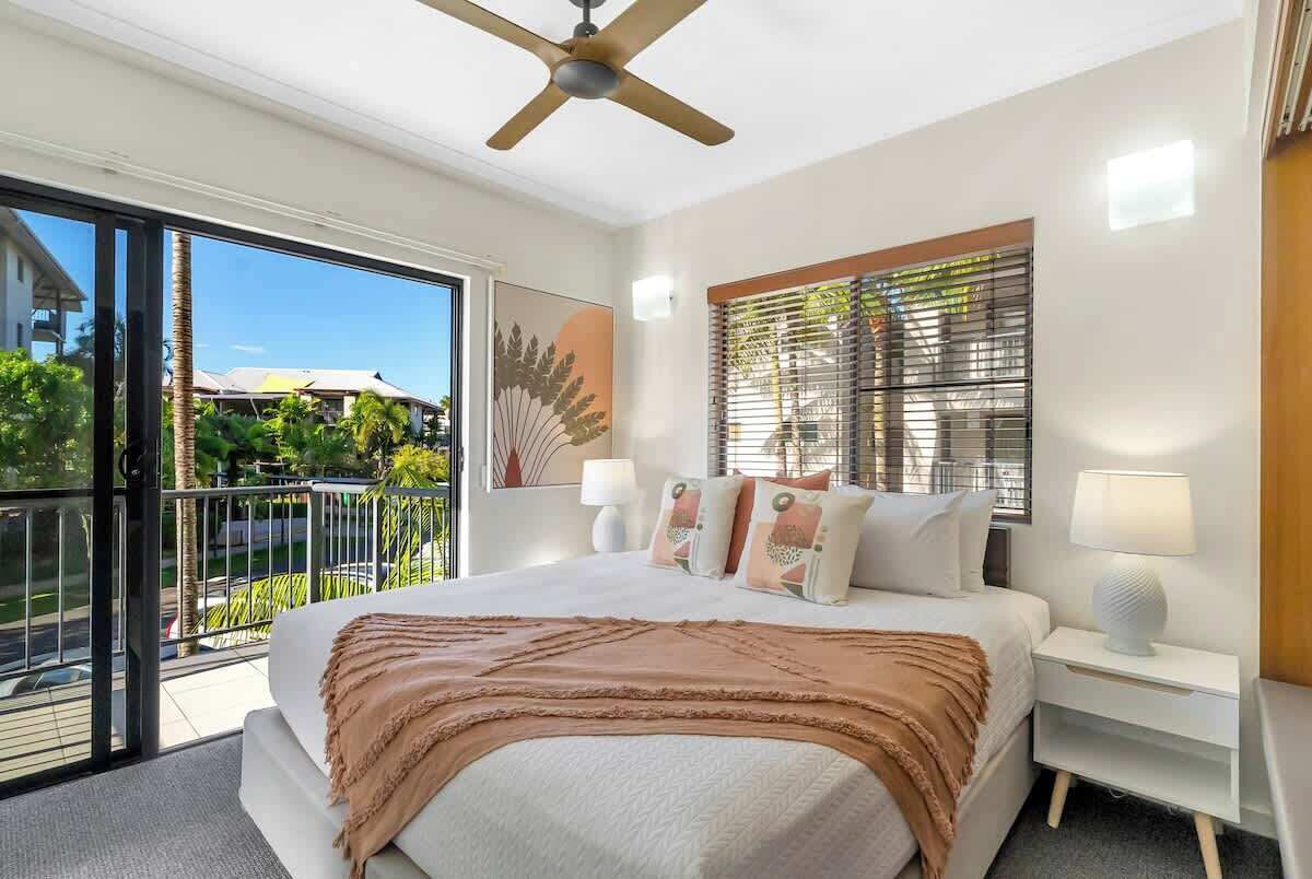Recharge in the king-sized bedroom, a peaceful retreat featuring split system air conditioning, a ceiling fan, and sliding doors that open onto a leafy private balcony.