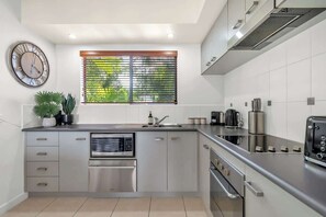 A modern kitchen with stainless steel appliances, a built-in oven, and a window with blinds.