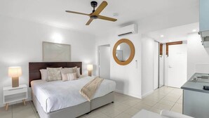 A bedroom with a bed, bedside tables, a ceiling fan, a mirror, and a door leading to a bathroom.