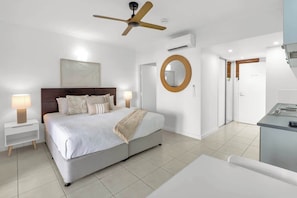 A bedroom with a bed, bedside tables, a ceiling fan, a mirror, and a door leading to a bathroom.