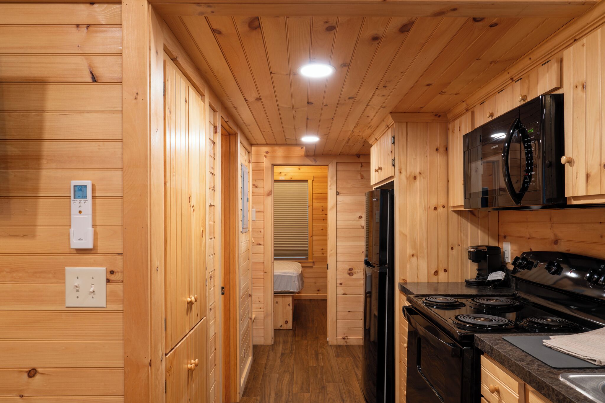 A compact kitchen with wooden walls, a black microwave, a stove, and a small window.