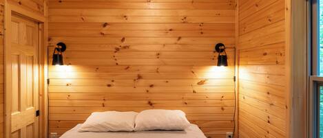 Una habitación con paneles de madera, una cama, dos lámparas de pared y un ventanal.