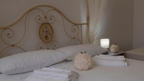 A neatly made bed with white linens, a decorative headboard, and a bedside lamp. - Double Room with Pool View (Lazio)