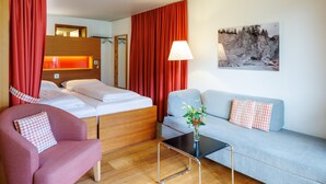 A hotel room with a bed, a sofa, a chair, a table, and a painting on the wall. - Hapimag Resort Andeer (Andeer)