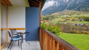 A balcony with a table and chairs, overlooking a mountainous landscape with fields and buildings. - Hapimag Resort Andeer (Andeer)