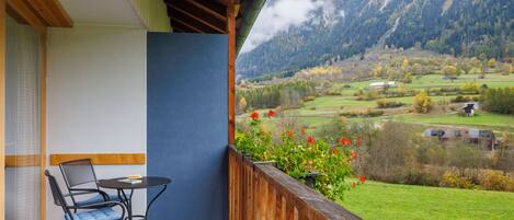 A balcony with a table and chairs, overlooking a mountainous landscape with fields and buildings.