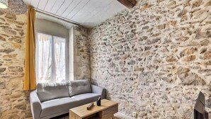 A cozy living room with a stone wall, a gray sofa, a wooden coffee table, and a TV.