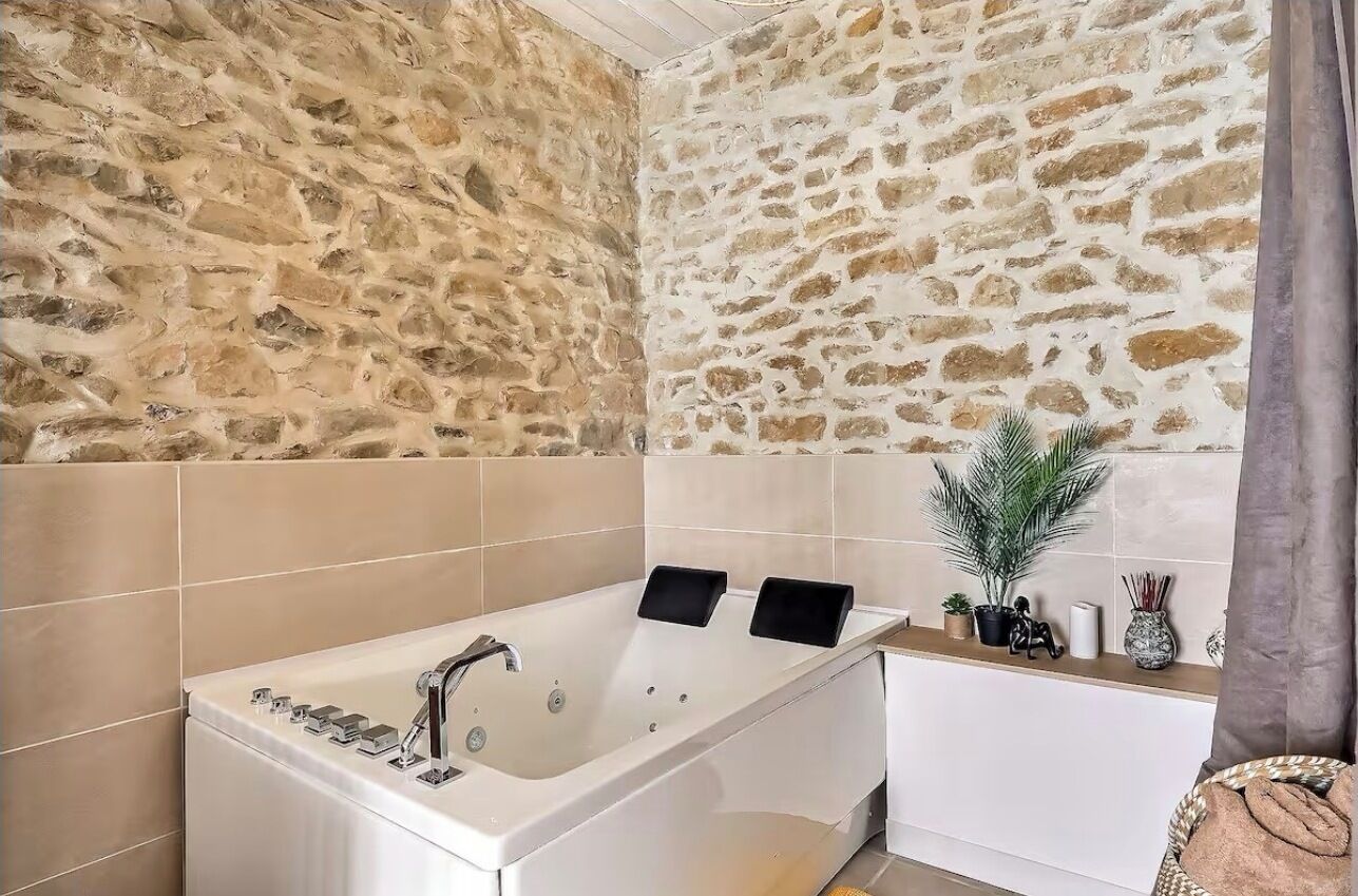 Un baño con pared de piedra, una bañera y un tocador con una planta y objetos decorativos.