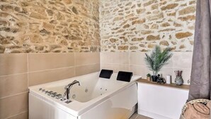 A bathroom with a stone wall, a bathtub, and a vanity with a plant and decorative items.